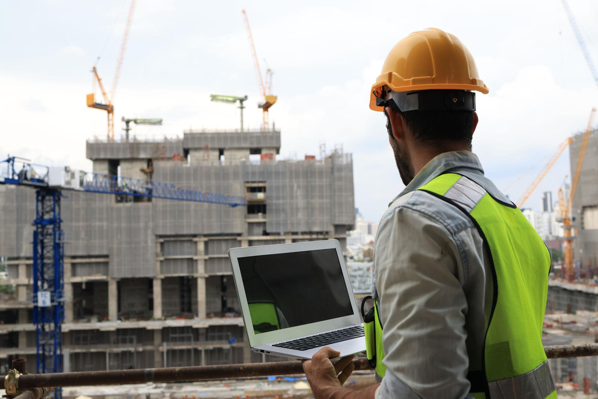 A project engineer at a construction site holds a laptop to track progress according to the plan. Monitoring progress is key to success. Our project engineer is on-site, armed with a laptop to ensure every milestone is achieved as planned.