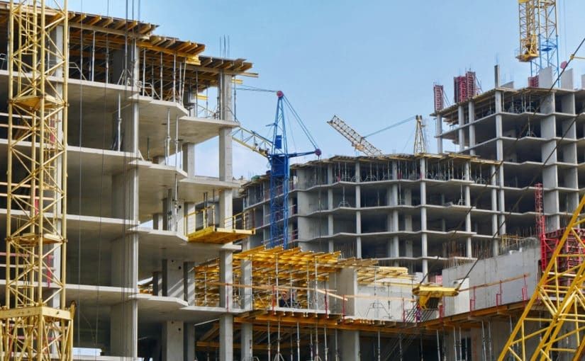 Construction site with multiple cranes and partially built concrete structures under a clear sky.