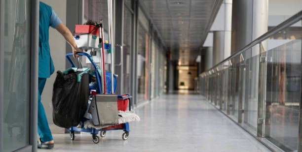 Person pushing a cleaning cart down a modern hallway with a glass railing and mop.