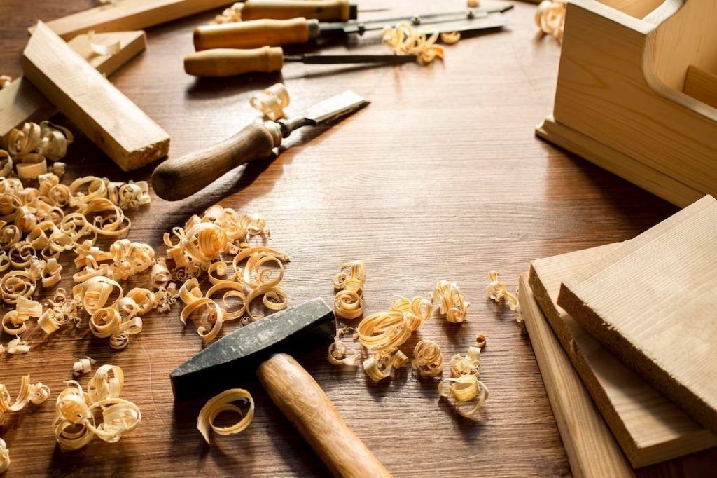 Woodworking tools and wood shavings on a wooden table with a hammer and chisel.