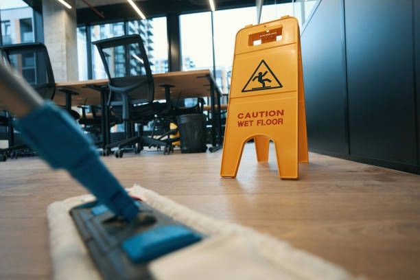 Mop cleaning an office floor with a caution wet floor sign nearby.