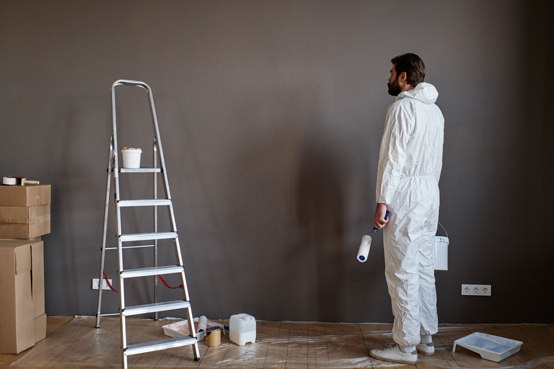 Joven caucásico con ropa protectora haciendo obras de renovación en nuevo apartamento que va a pintar paredes