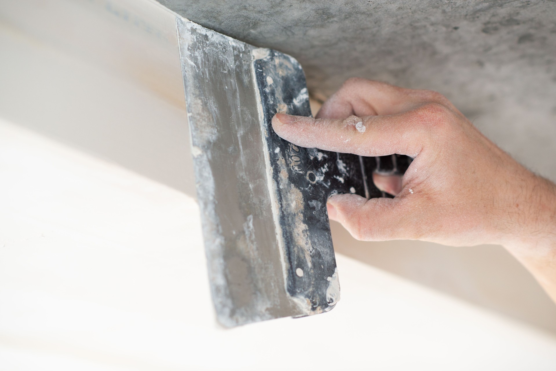 Trabajador putts techo de placas de yeso en nuevo apartamento. Repairman trabaja con placas de yeso, yeso pared de piedra seca, mejora del hogar. Un hombre hace reparaciones en casa. Cuchillo masilla en mano masculina. Trabajo a mano.